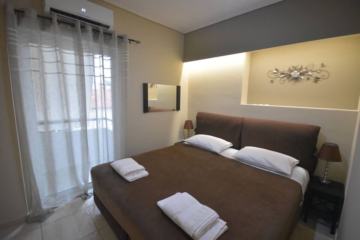 Een hotelkamer met een groot bed, twee nachtkastjes met lampen, een spiegel aan de muur en een decoratief kunstwerk.