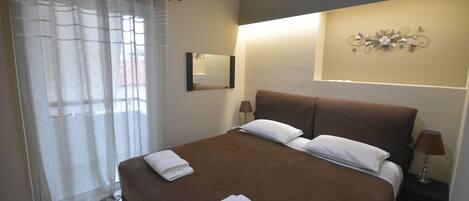 A hotel room with a large bed, two bedside tables with lamps, a wall-mounted mirror, and a decorative wall piece.