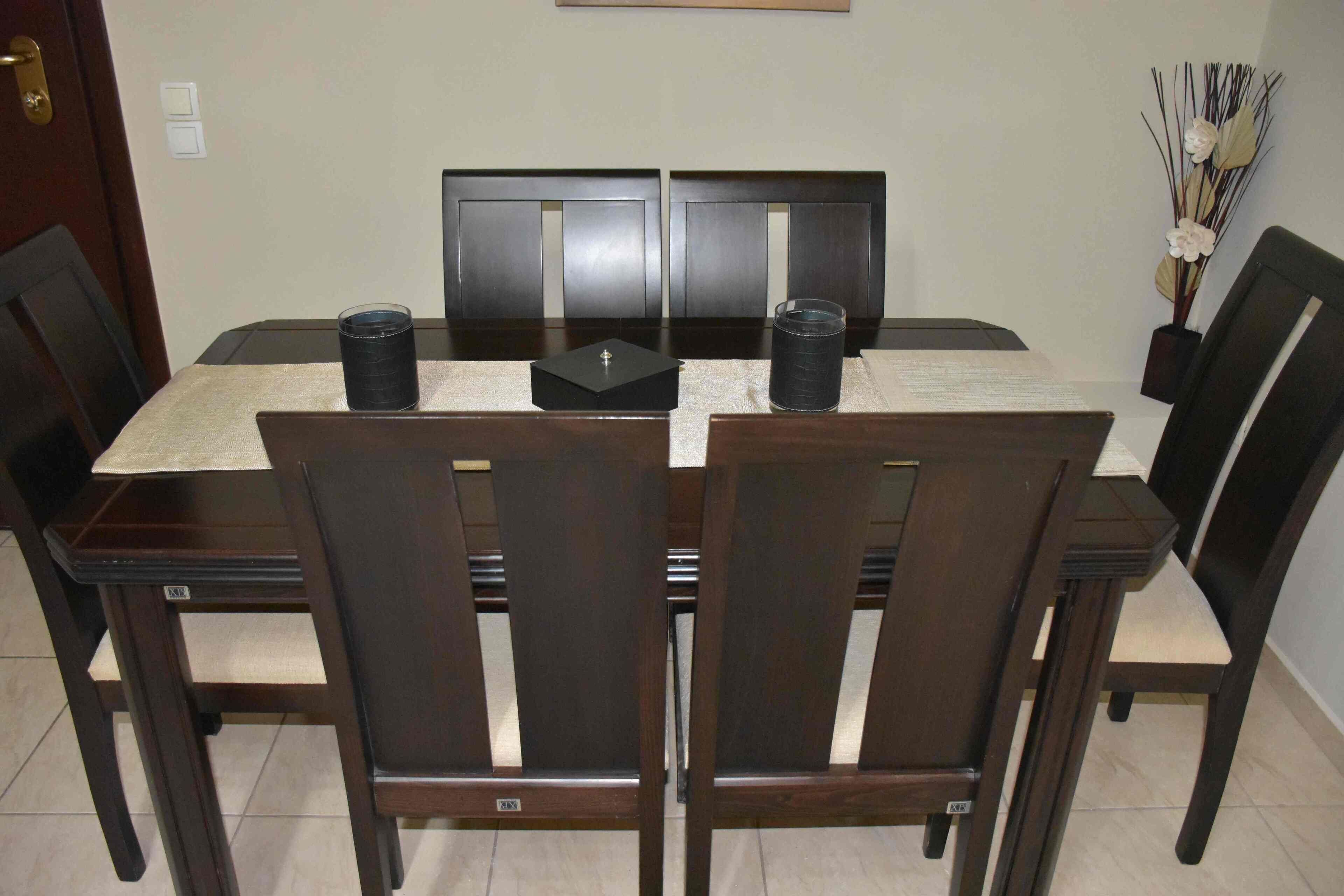 Una mesa de comedor con cuatro sillas, cada una con un asiento acolchado y estructura de madera oscura. Hay dos candelabros negros sobre la mesa.
