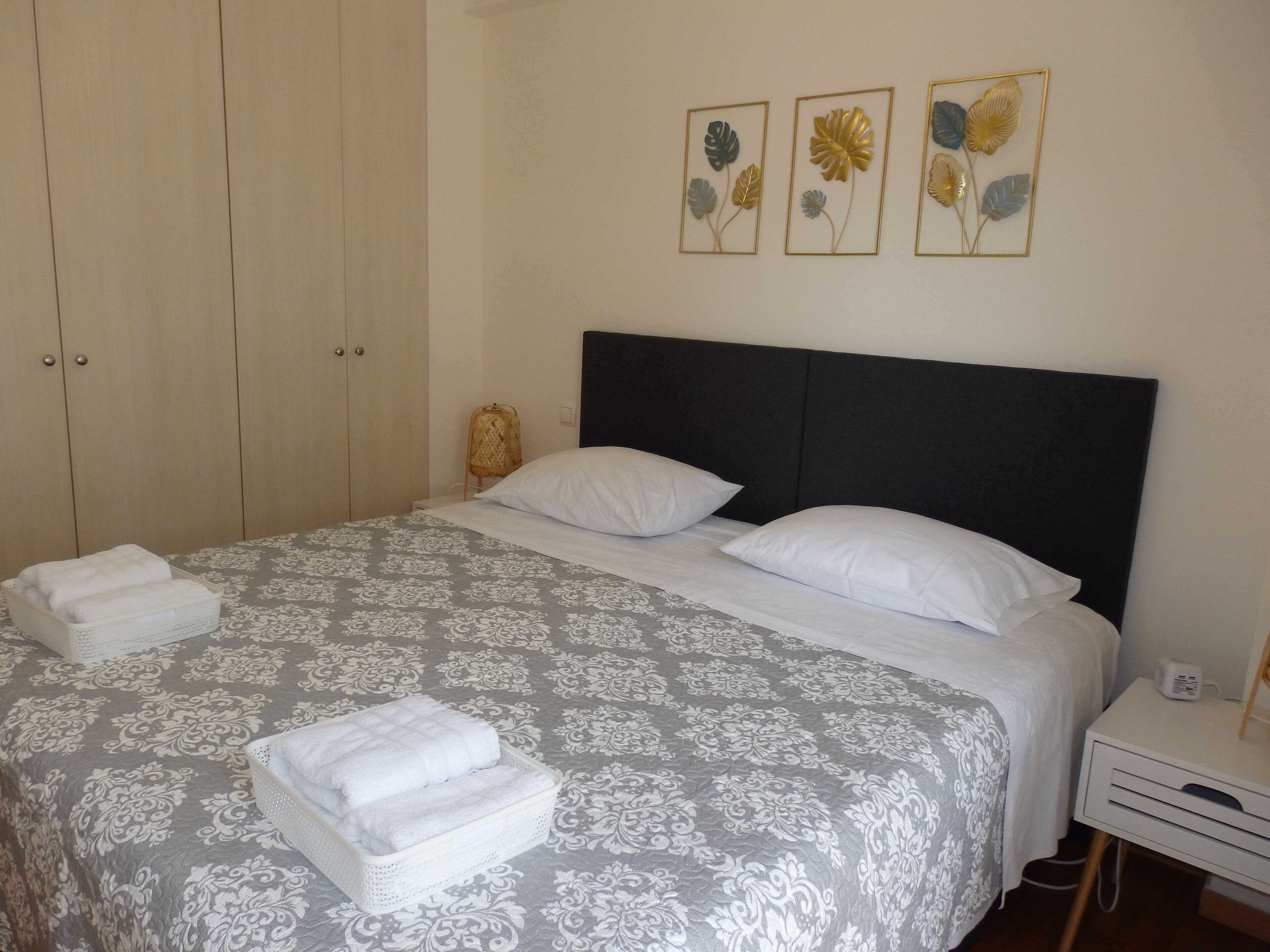 Een net opgemaakt bed met een beddekleed met patroon, twee kussens en een nachtkastje met een lamp.