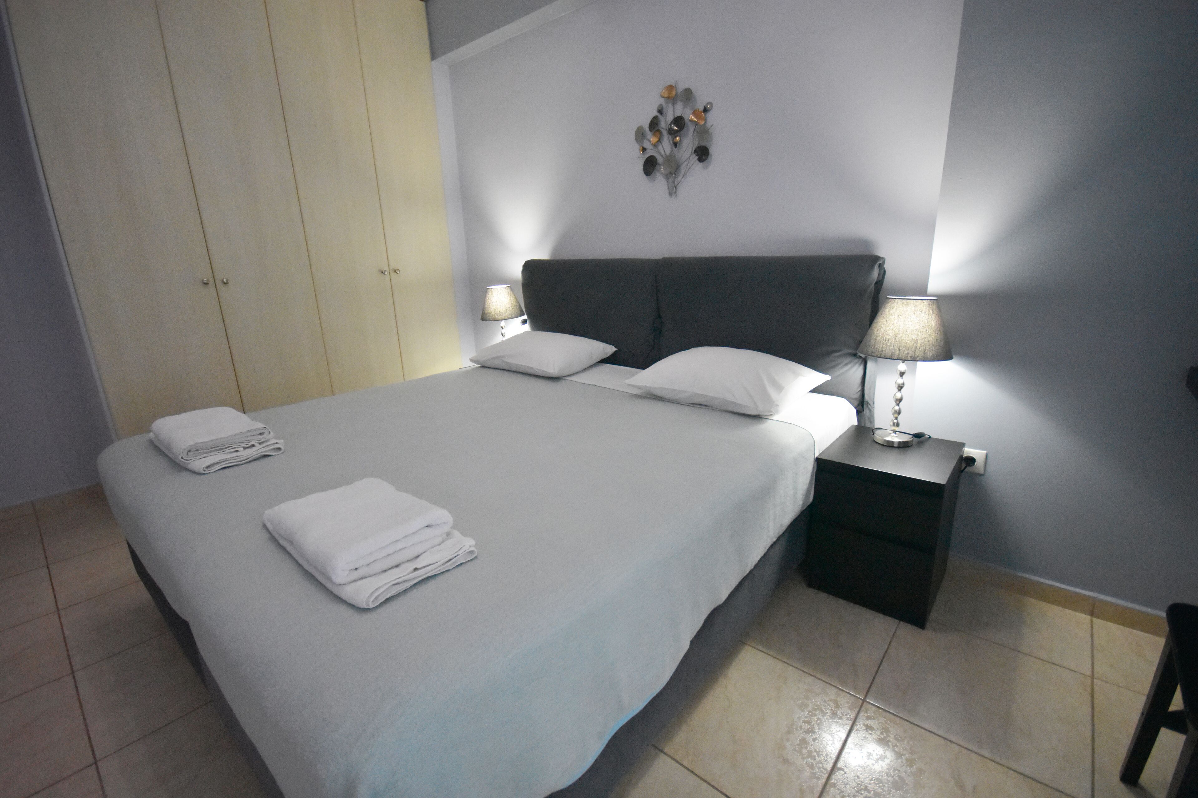 A neatly made bed with white linens and pillows, a bedside table with a lamp, and a wardrobe with sliding doors.