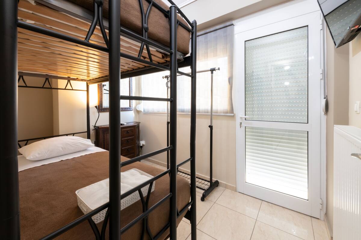 Een stapelbed met een houten hoofdbord, een nachtkastje met een lamp, en een schuifdeur naar buiten.