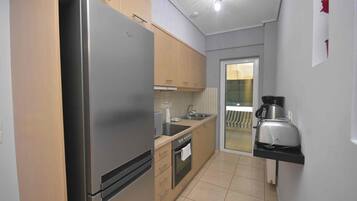 A compact kitchen with a stainless steel refrigerator, wooden cabinets, a built-in oven, and a coffee maker on the countertop.