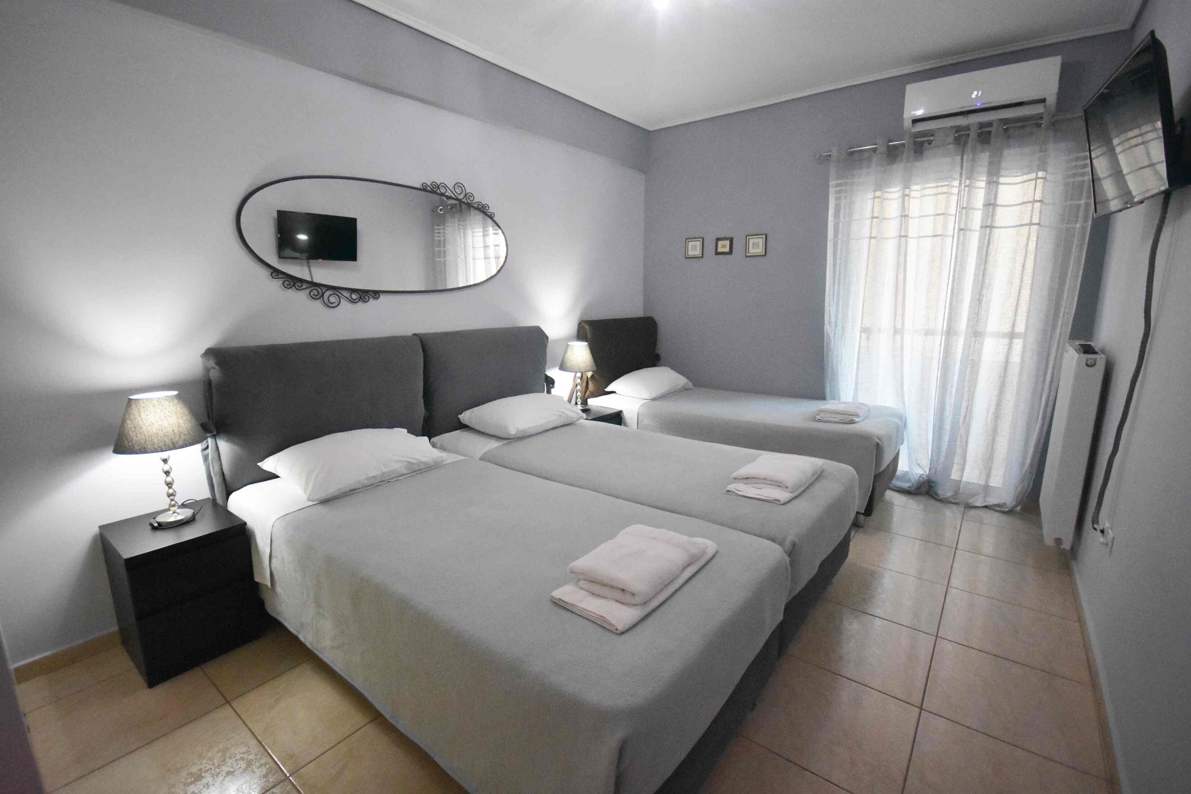 Habitación de hotel con dos camas, un televisor montado en la pared, un aire acondicionado y una ventana con cortinas.