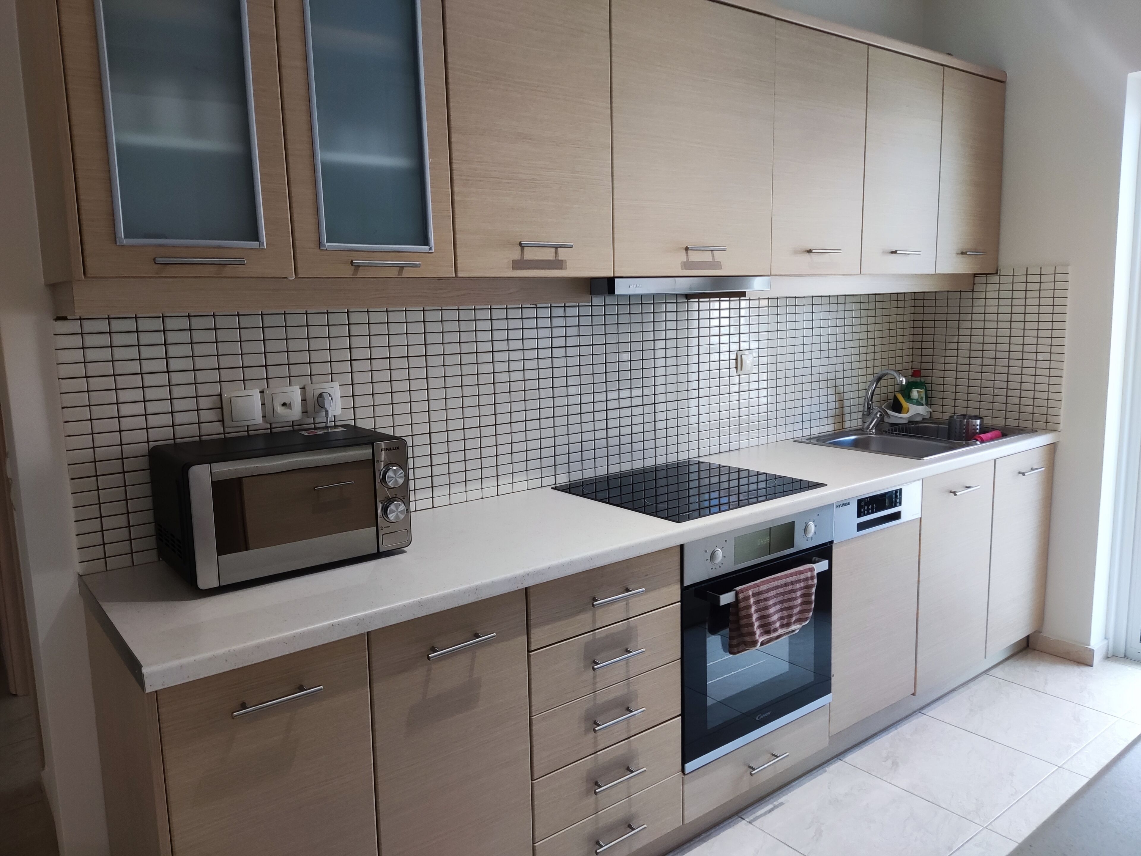 Una cocina moderna con armarios de madera, horno empotrado, microondas y un lavamanos.