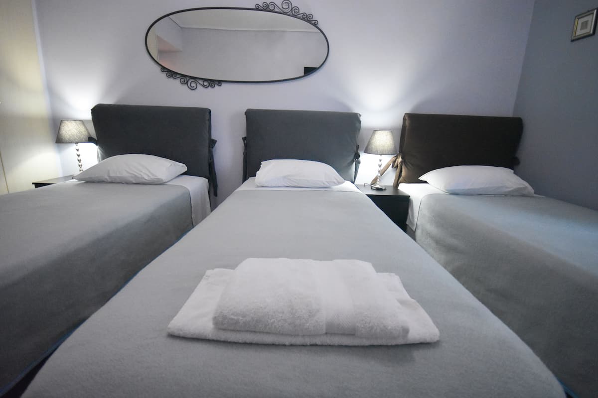Een hotelkamer met drie eenpersoonsbedden, elk met een kussen en nachtkastje. Een grote spiegel is aan de muur boven de bedden bevestigd.
