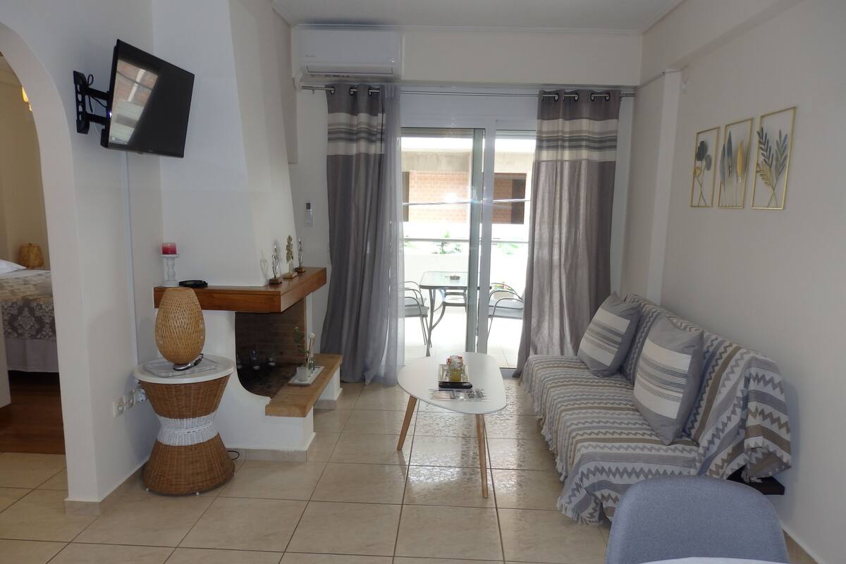 Een moderne woonkamer met een bank, een bijzettafeltje, een aan de muur bevestigde televisie en een balkon met gordijnen.