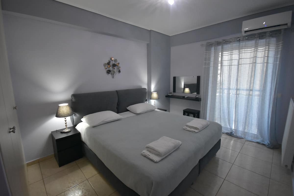 Een moderne slaapkamer met een groot bed, bedlampen, een flatscreen televisie en een airconditioning.