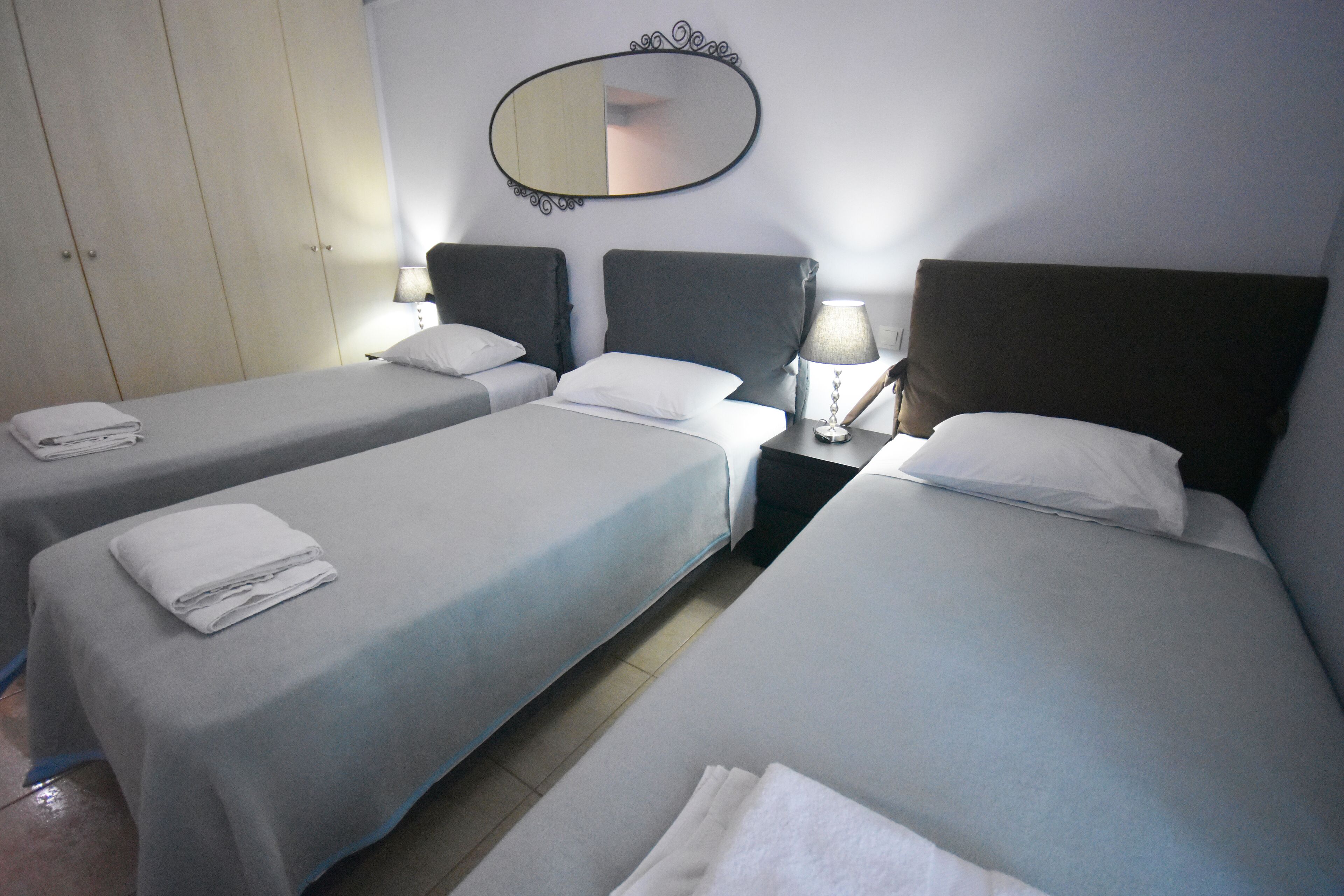 Une chambre d’hôtel avec deux lits simples, une armoire, un miroir et des lampes de chevet.