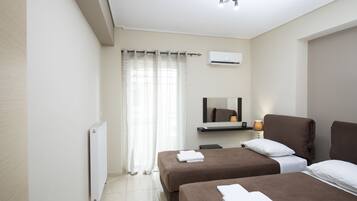Una camera d'albergo con due letti, una finestra con tende, un condizionatore d'aria, uno specchio e un comodino con lampada.