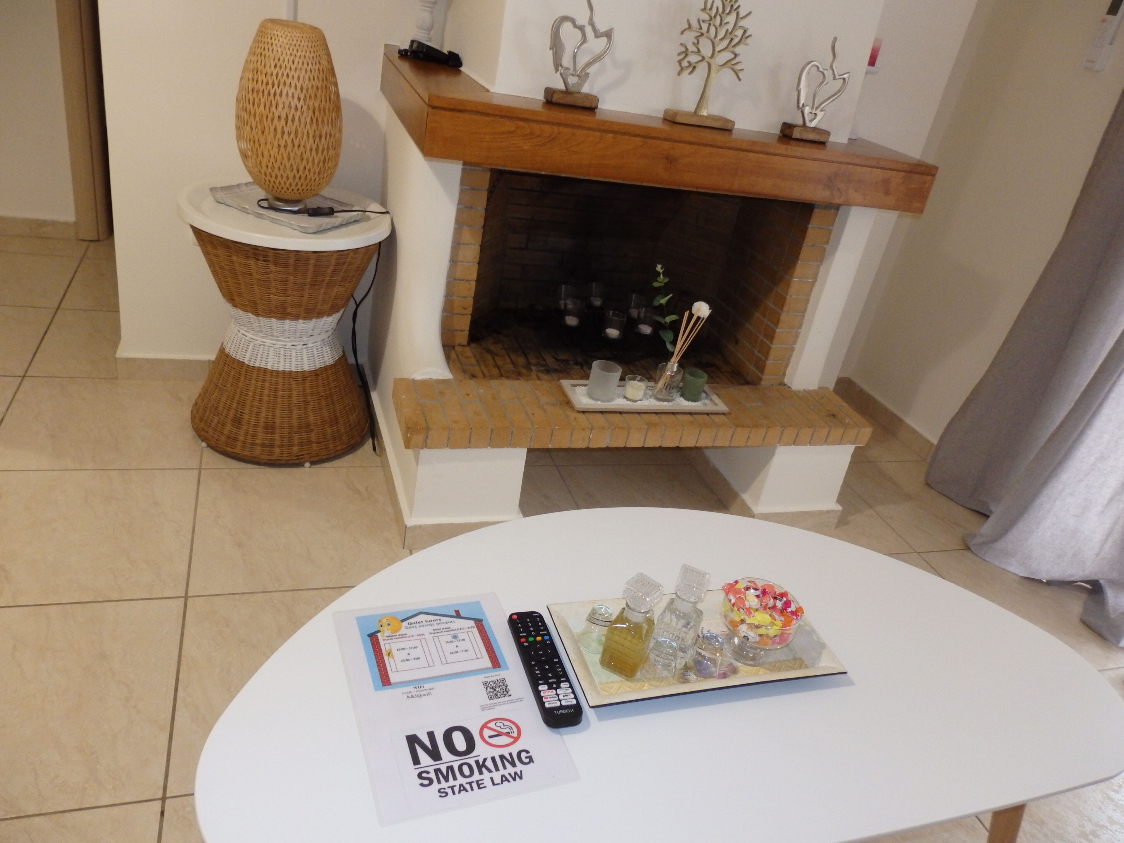A hotel room with a white round table, a fireplace, a wicker stool, and a "No Smoking" sign.