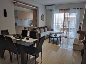 A modern living room with a dining area, a kitchen, and a balcony with a view. - A&J Apartments or Rooms athens airport (Markopoulo Mesogaias)