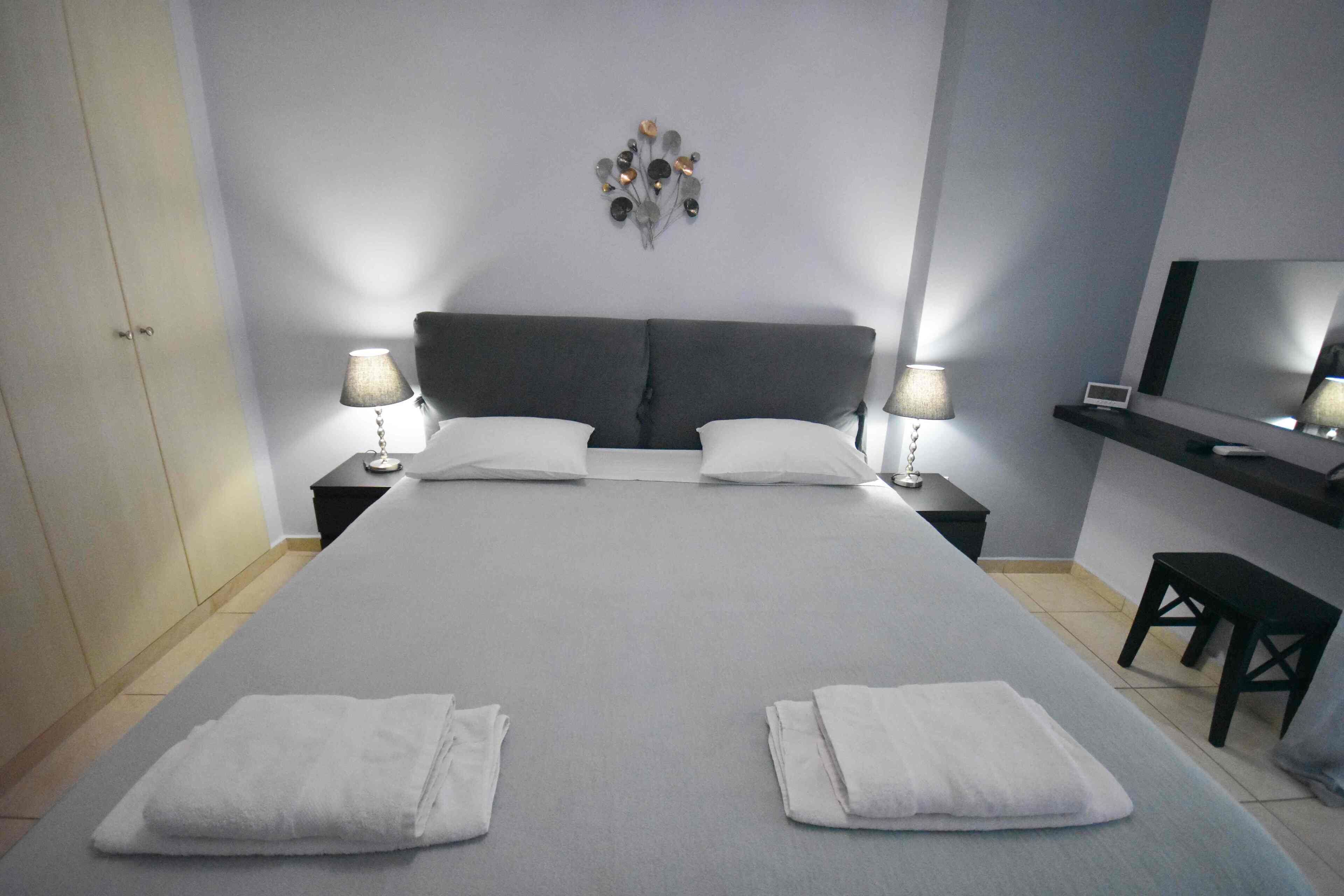 A hotel room with a large bed, two bedside tables with lamps, a TV on a stand, and a wall decoration.