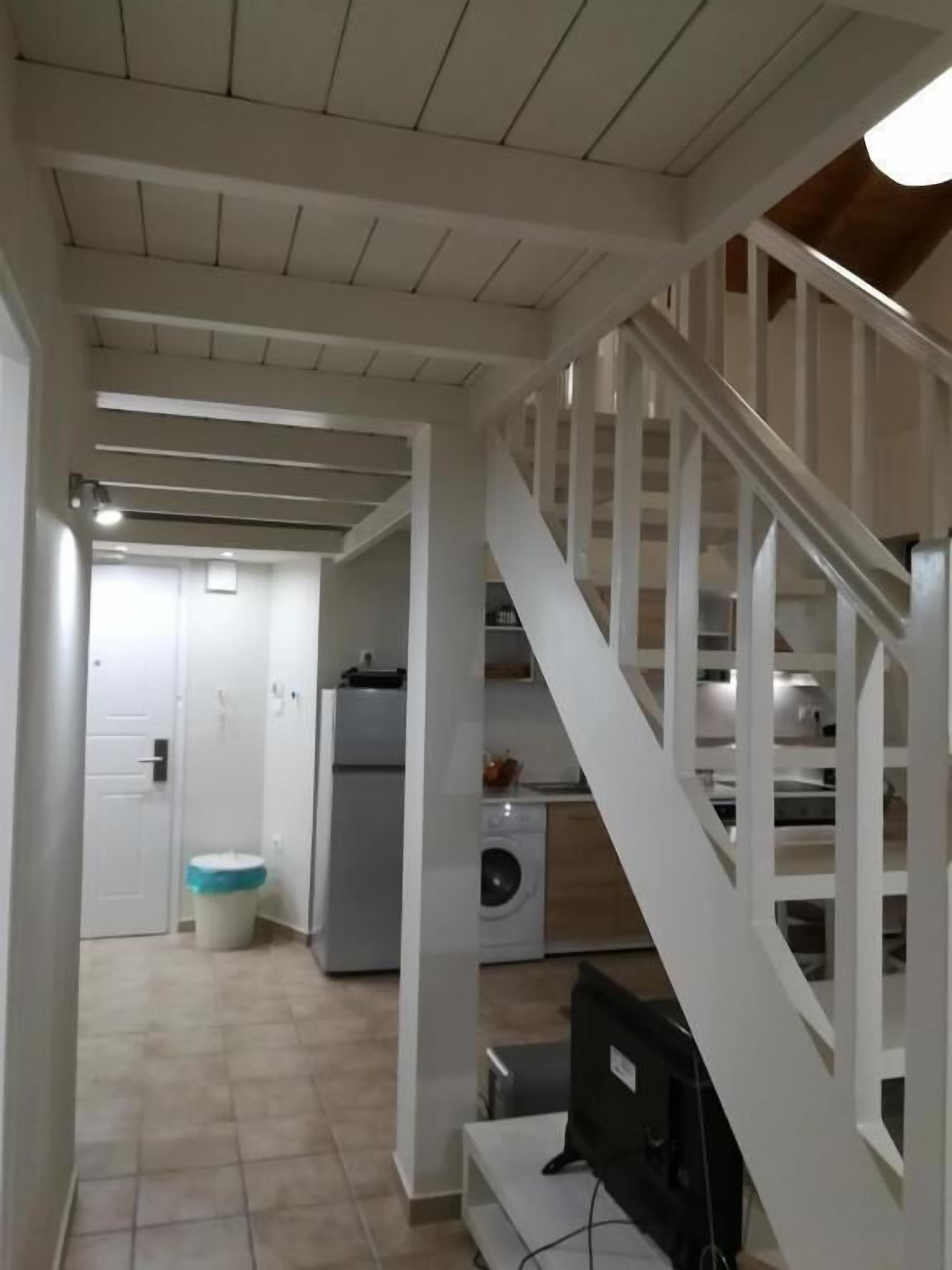 Un espacio habitable amplio con una escalera que sube a un segundo piso, una cocina con lavadora y una puerta que da a otra habitación.
