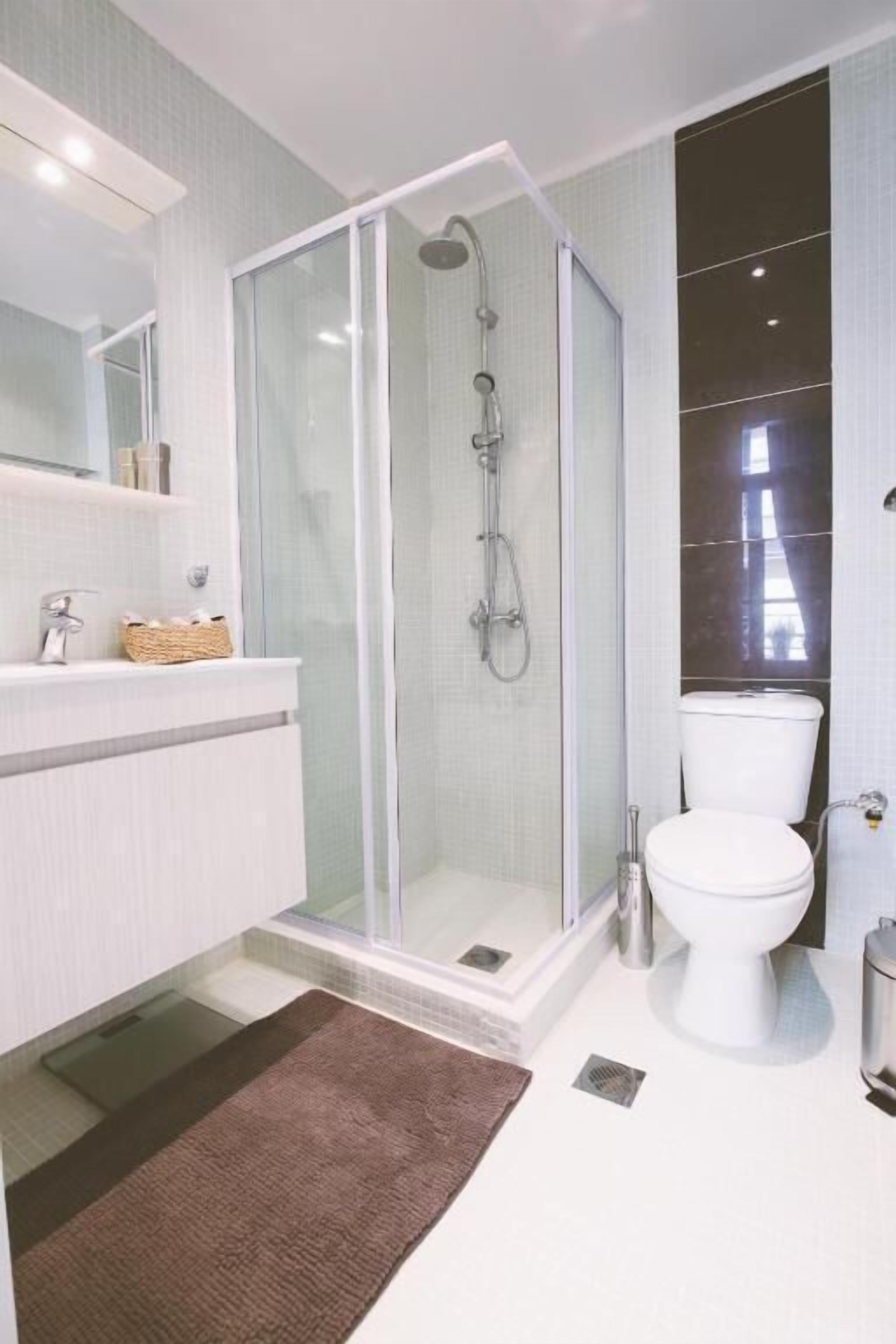 Une salle de bain moderne avec une douche à parois de verre, des toilettes blanches et un meuble-lavabo doté d’un miroir et d’un panier.