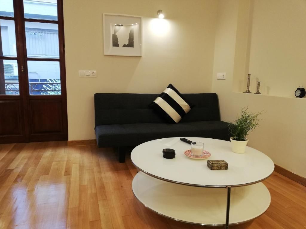 A living room with a black sofa, a white round table, a potted plant, and a framed picture on the wall.