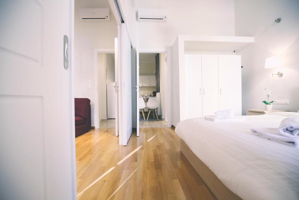 Une chambre d’hôtel avec un plancher en bois, un lit avec du linge de maison blanc, un bureau avec une chaise et une petite table avec une plante.