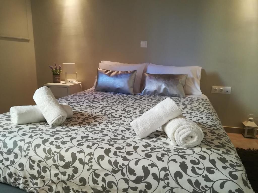 Un lit bien fait, recouvert d’une couvre-lit à motifs, avec deux serviettes enroulées et une table de chevet sur laquelle se trouvent une lampe et une petite plante.