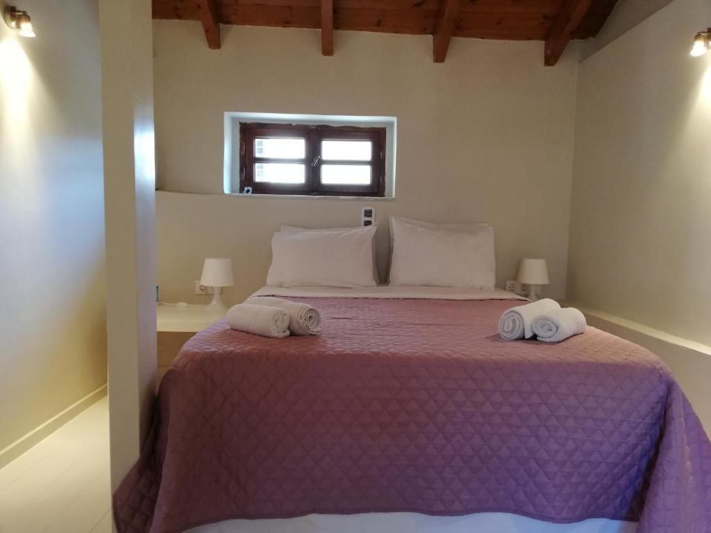 A bedroom with a bed, two bedside lamps, a window, and a rolled towel on the bed.