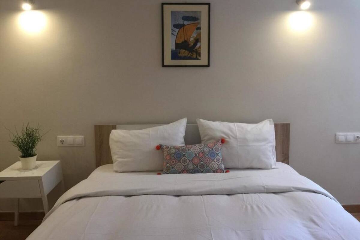 Ein Schlafzimmer mit einem Bett, zwei Nachttischen, einer Topfpflanze und einem gerahmten Kunstwerk an der Wand.