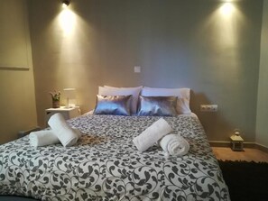 A neatly made bed with patterned bedding, two pillows, and rolled towels on a bedside table. - Central Apartments in Psiri (Athens)