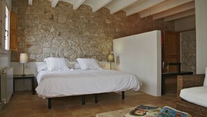 A bedroom with a stone wall, a bed with white bedding, two bedside tables with lamps, and a wicker chair.