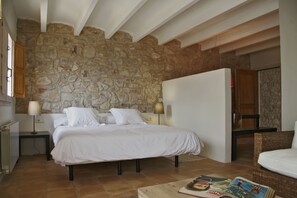 A bedroom with a stone wall, a bed with white bedding, two bedside tables with lamps, and a wicker chair.