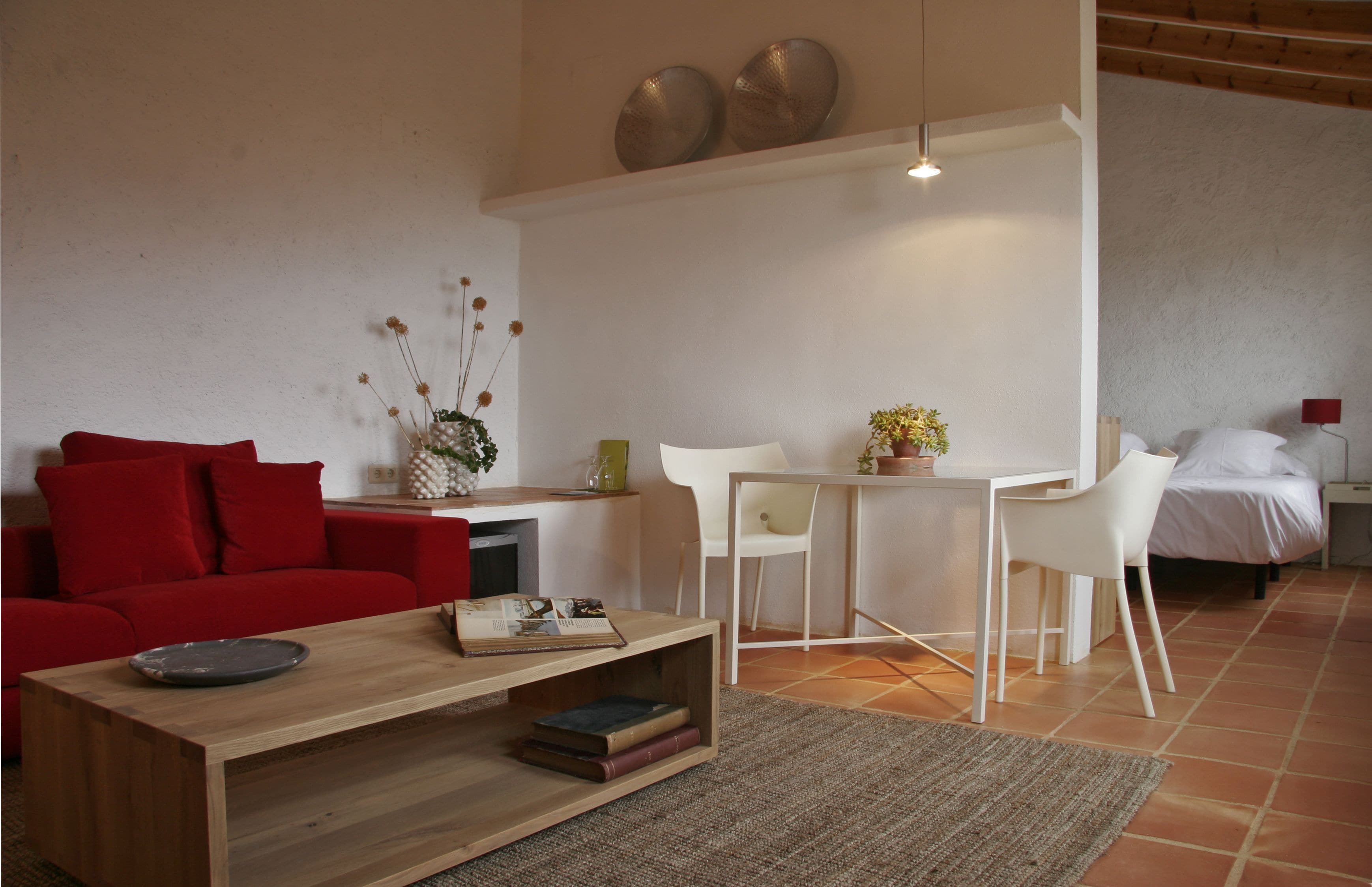 A modern living room with a red sofa, a wooden coffee table, and a dining area with white chairs and a small table.