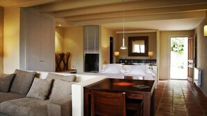 A modern hotel room with a sofa, dining table, and a kitchen area visible through an open door. - Aldea Roqueta Hotel Rural (Culla)
