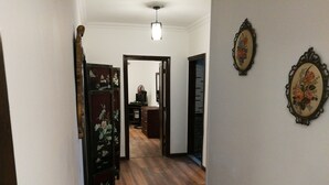 Een gang met houten vloer, een bureau met een computer, en twee wanddecoraties met bloemen.