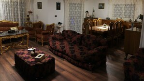 Een woonkamer met een bank, fauteuils, een salontafel en een eethoek met een tafel en stoelen.