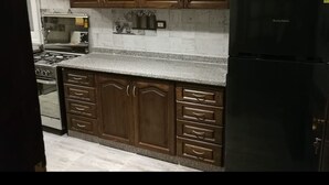 Een keuken met donkere houten kastjes, een granieten aanrecht, een zwarte koelkast en roestvrijstalen apparatuur.