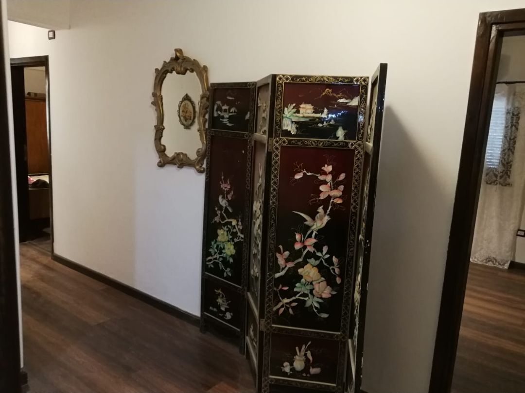 A hallway with a dark wooden floor, a white wall, and a decorative mirror with a gold frame.