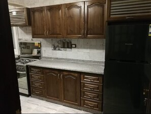 A kitchen with dark wooden cabinets, a granite countertop, a black refrigerator, and stainless steel appliances. - Luxury three bedrooms apartment in degla maadi (Cairo)