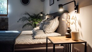 A bedroom with a bed, a bedside table, a lamp, a potted plant, and a window. - Csendeskert Apartments (Balatonalmadi)