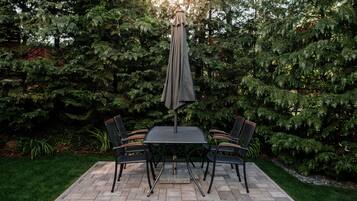 A patio with a table and chairs, surrounded by a lush garden and tall trees.