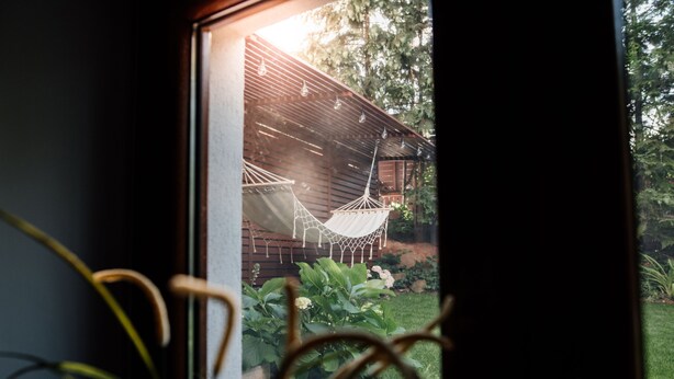 A view through a window of a wooden structure with a hammock and hanging lights. - Csendeskert Apartments (Balatonalmadi)