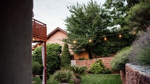 A well-maintained garden with a stone wall, potted plants, and a wooden pergola. - Csendeskert Apartments (Balatonalmadi)