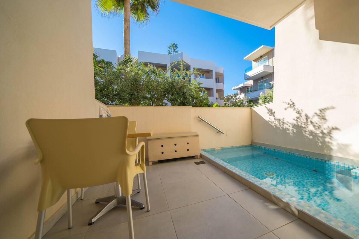 A small balcony with a pool, a chair, and a table.