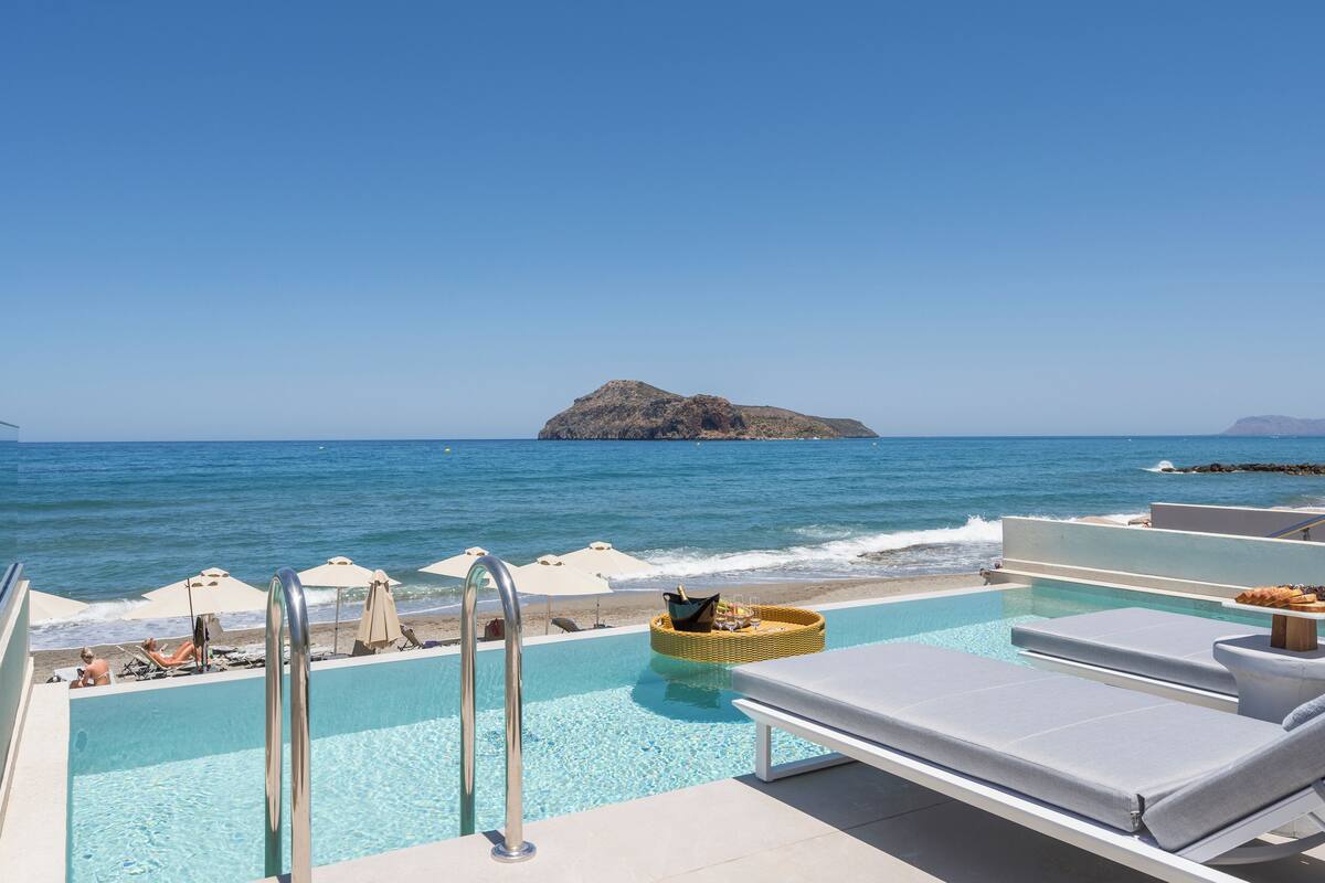 A poolside area with lounge chairs, a wicker basket, and a view of the ocean and a rocky island.