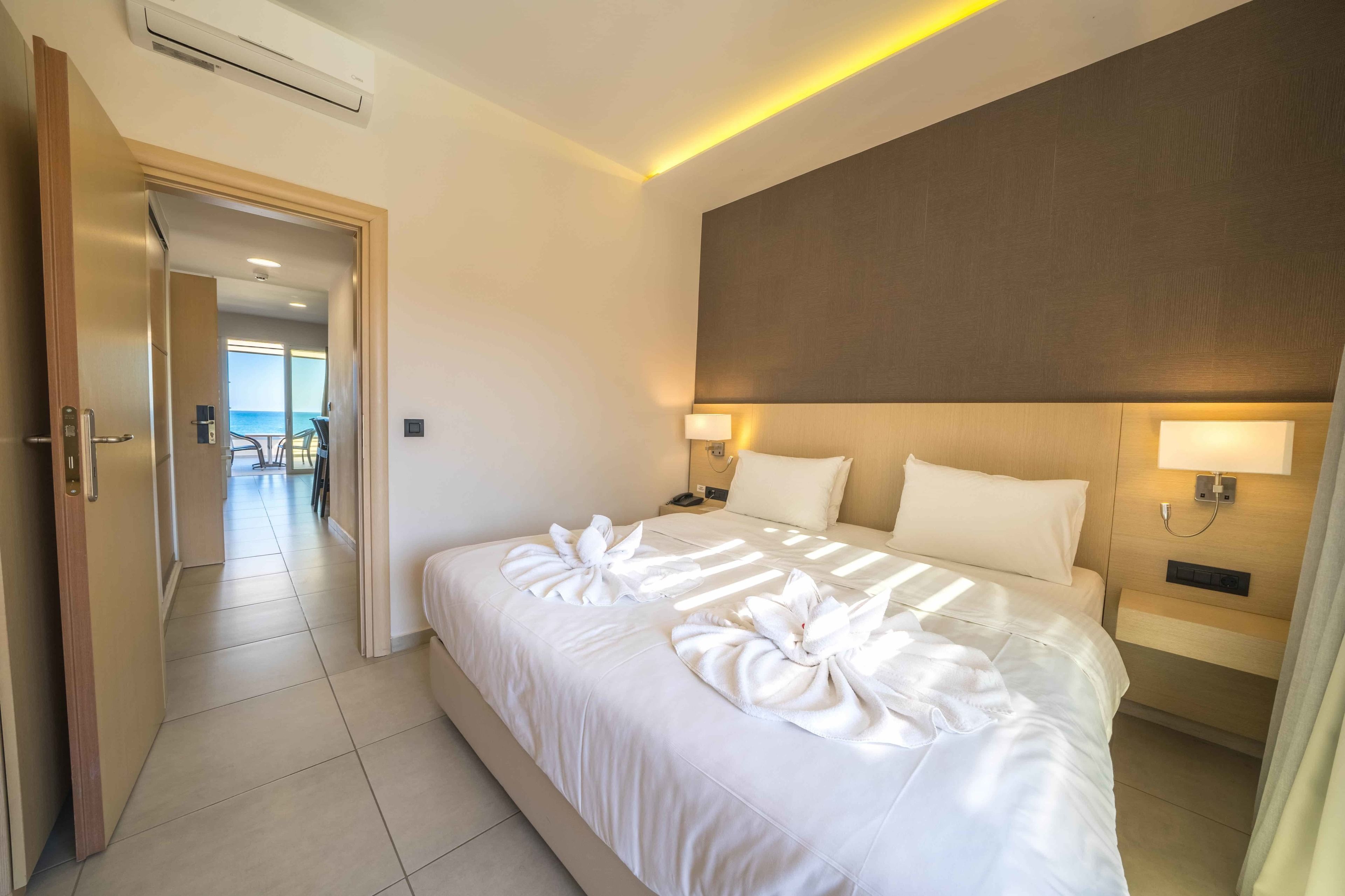 A hotel room with a large bed, two bedside lamps, and a view of the sea through a door.
