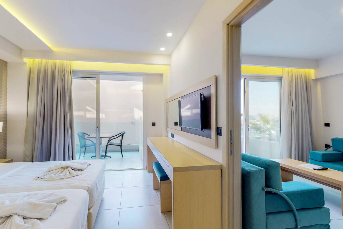 A hotel room with a bed, a desk, a chair, a TV, and a balcony with a chair.