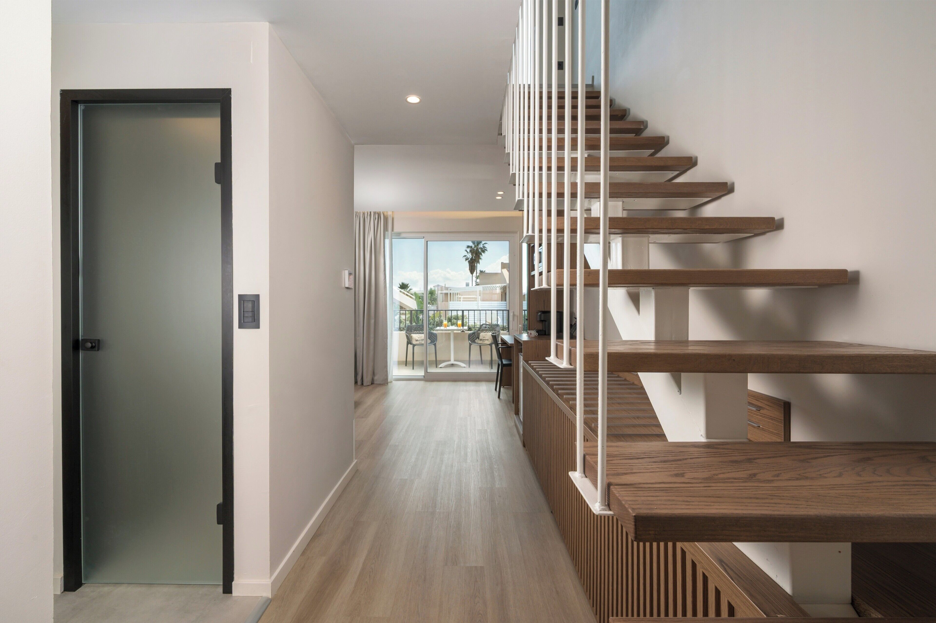 Un intérieur moderne avec un escalier en bois, une porte en verre et une vue sur un espace extérieur.