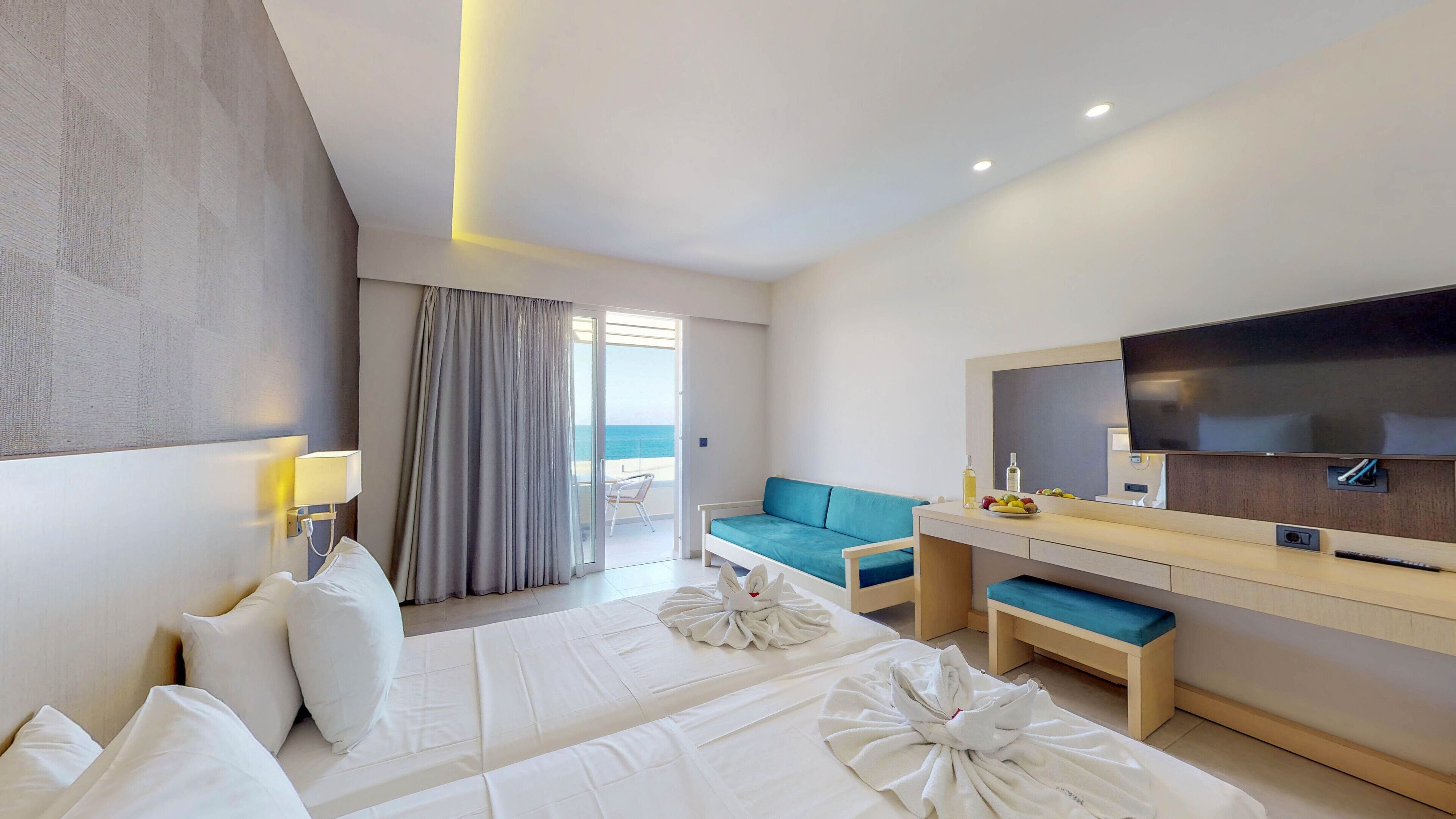 A hotel room with a bed, a sofa, a TV, and a view of the sea.