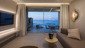 Una sala moderna con un televisor grande, un sofá, una mesa de centro con una botella de champán y vista al océano a través de puertas de vidrio del piso al techo.