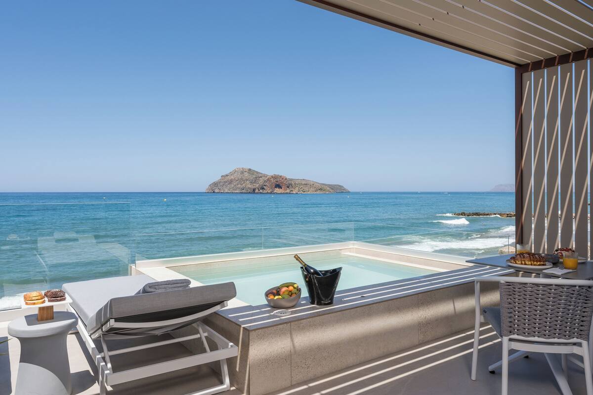 A balcony with a view of the sea, a hot tub, and a table with food and drinks.