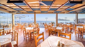 Un restaurante con mesas y sillas de madera, ventanas amplias y vista al mar.