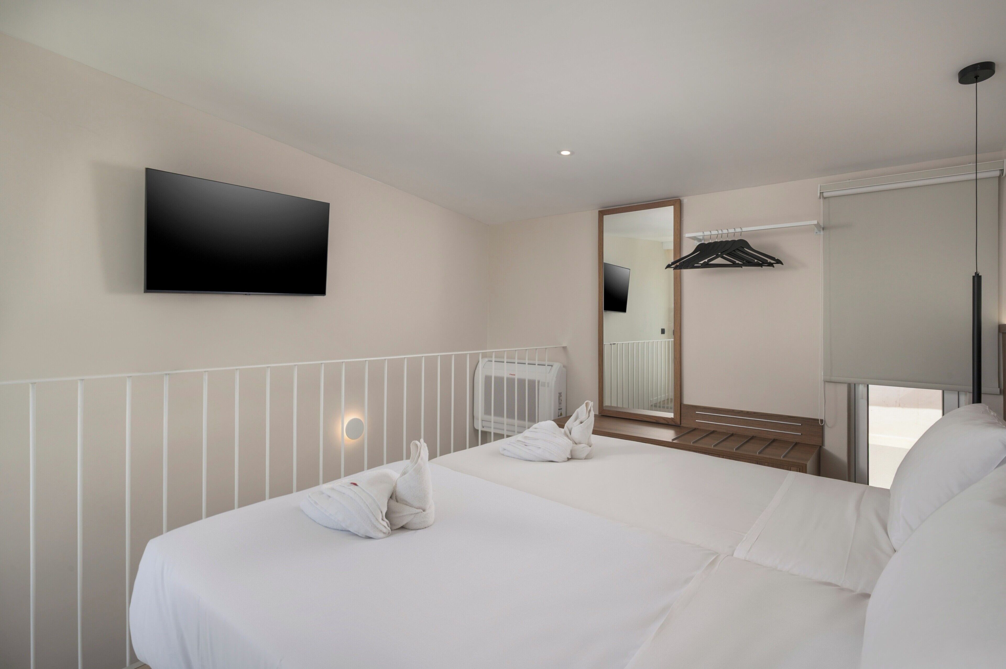 A hotel room with a large bed, a flat-screen TV mounted on the wall, a radiator, and a mirror.