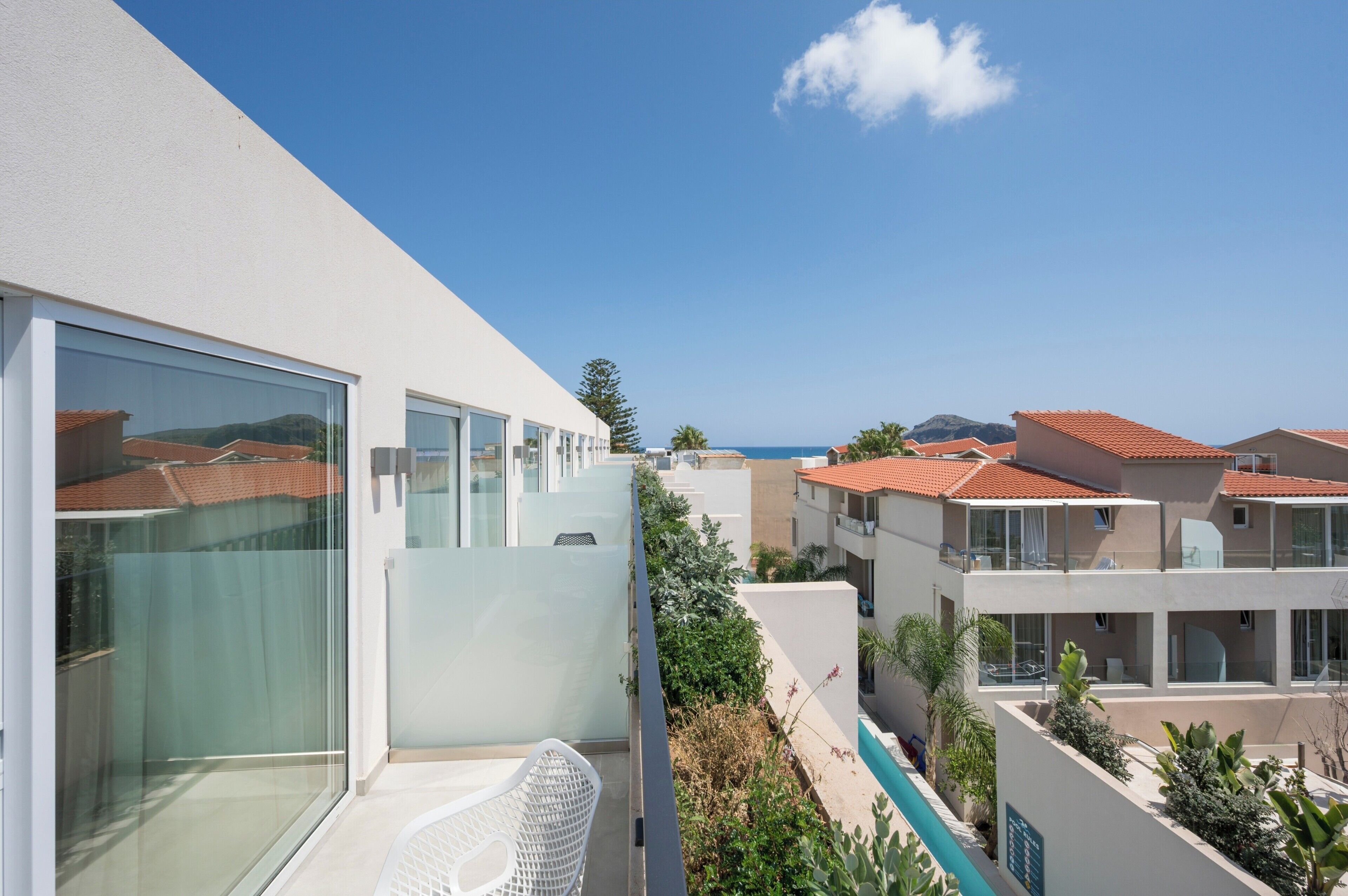 Ein modernes Hotel mit großen Fenstern, einem Balkon mit einem Stuhl und Meerblick.