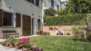 Ein Innenhof mit Rasenfläche, Blumentöpfen, einer Bank und Gartenmöbeln.